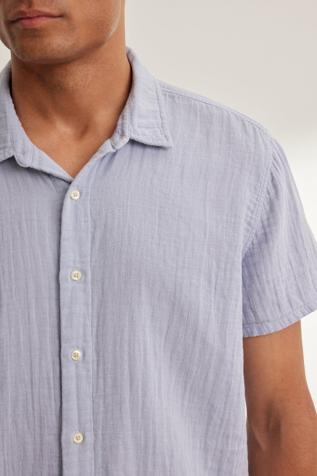   A person is shown from shoulders to mid-torso wearing the CHRISTIAN COTTON GAUZE BUTTON-UP SHIRT by Velvet by Graham & Spencer, a light blue, short-sleeve cotton shirt, against a plain background. 