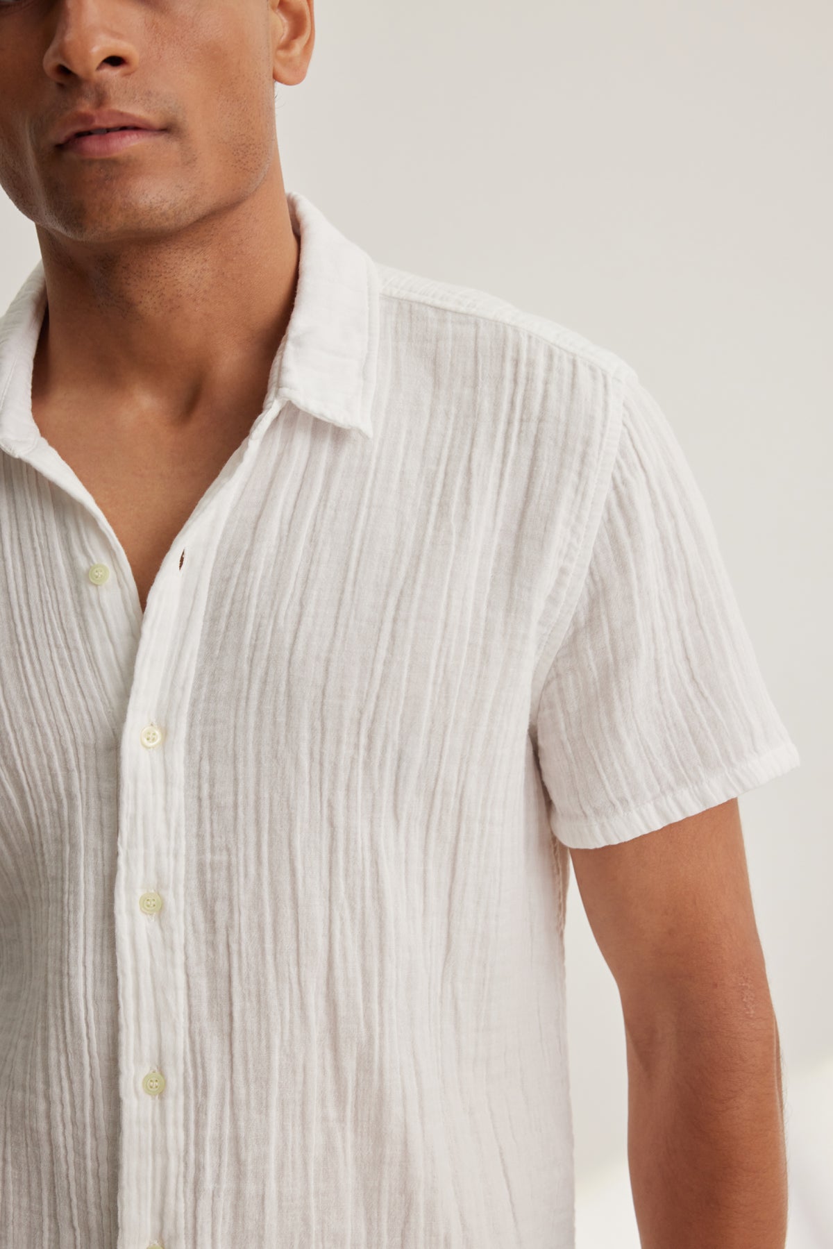 A man wears the CHRISTIAN COTTON GAUZE BUTTON-UP SHIRT by Velvet by Graham & Spencer, a white short-sleeved shirt with a subtle texture, standing against a plain light background.-39152366026945