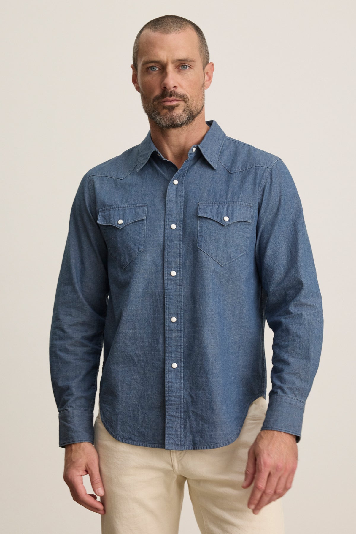 A man with short hair and a beard wears the Velvet by Graham & Spencer CODY BUTTON-UP SHIRT and light-colored pants, standing against a plain background.