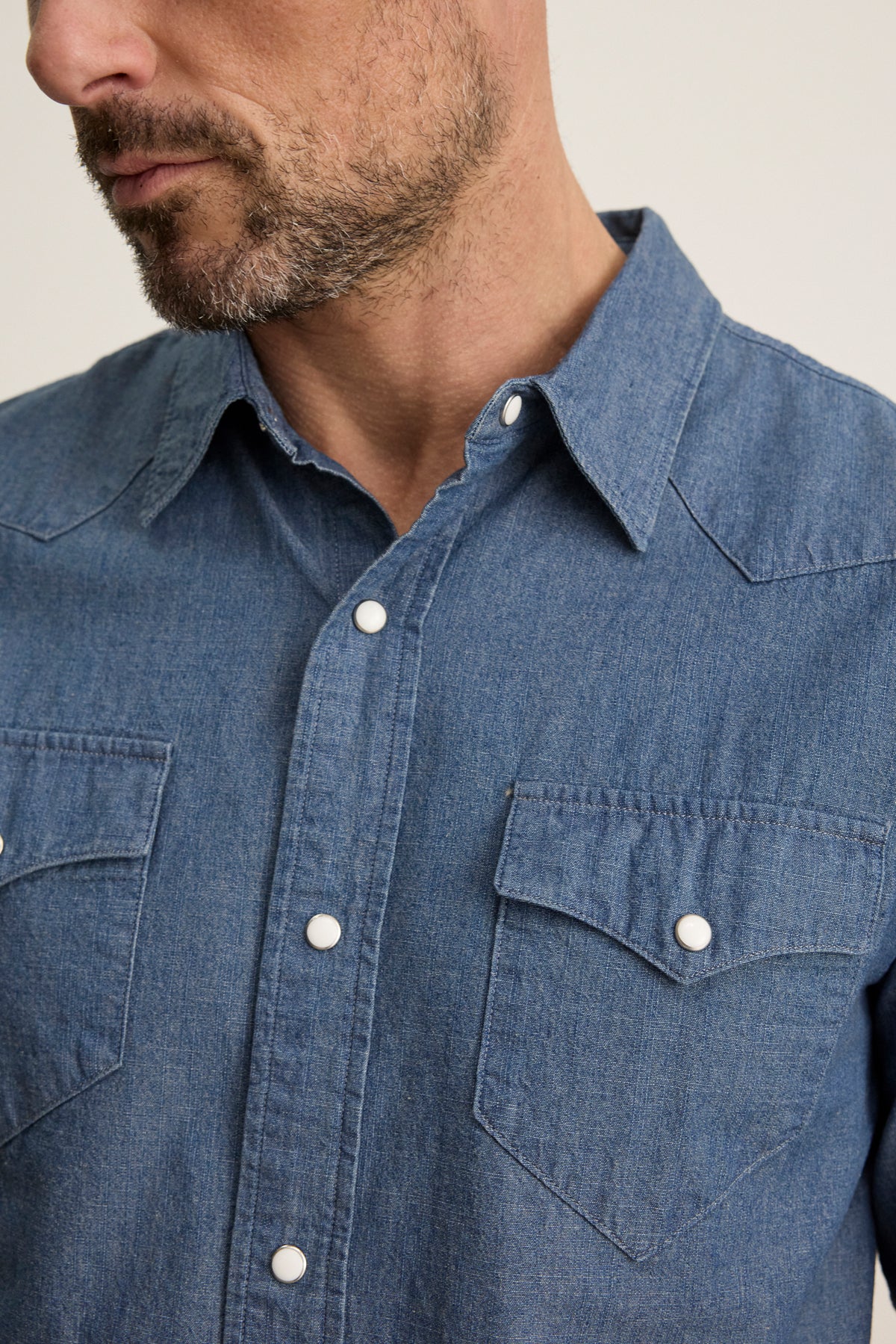 A man wears the CODY BUTTON-UP SHIRT by Velvet by Graham & Spencer, a tailored-fit blue denim shirt with two chest pockets and white snap buttons in classic Western style.-39934272831681