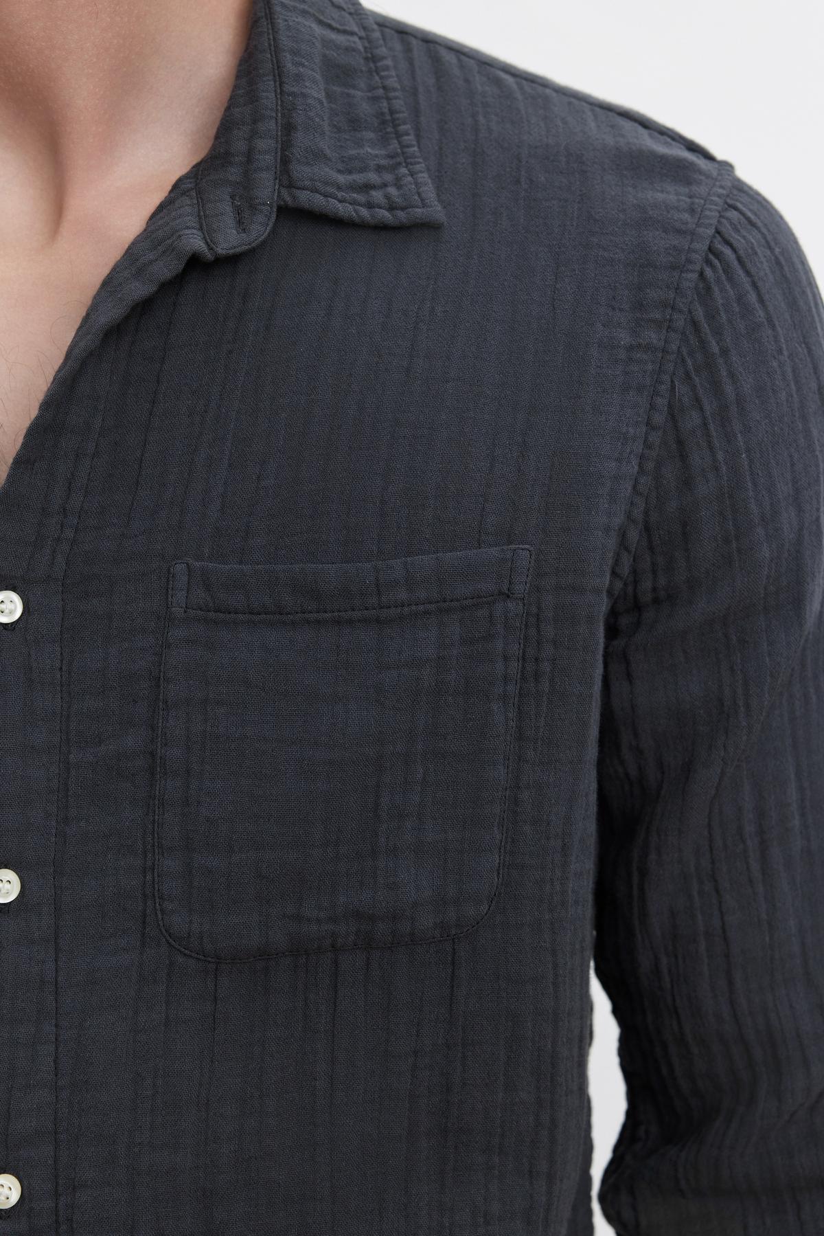   A person wearing a dark grey ELTON COTTON GAUZE BUTTON-UP SHIRT from Velvet by Graham & Spencer made from textured cotton gauze woven fabric with a chest pocket, viewed from the chest up. A versatile choice for various occasions. 