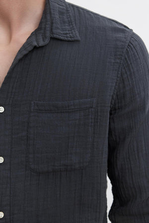 A person wearing a dark grey ELTON COTTON GAUZE BUTTON-UP SHIRT from Velvet by Graham & Spencer made from textured cotton gauze woven fabric with a chest pocket, viewed from the chest up. A versatile choice for various occasions.