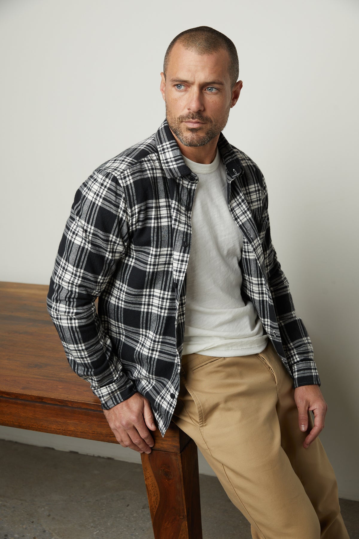   A man in a Velvet by Graham & Spencer Freddy Plaid Shirt leaning on a wooden table. 