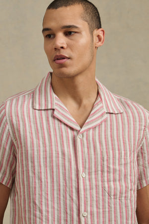 A person wearing the HOBBS SHIRT by Velvet by Graham & Spencer, a short-sleeve button-up with pink and white vertical stripes, stands against a plain background.
