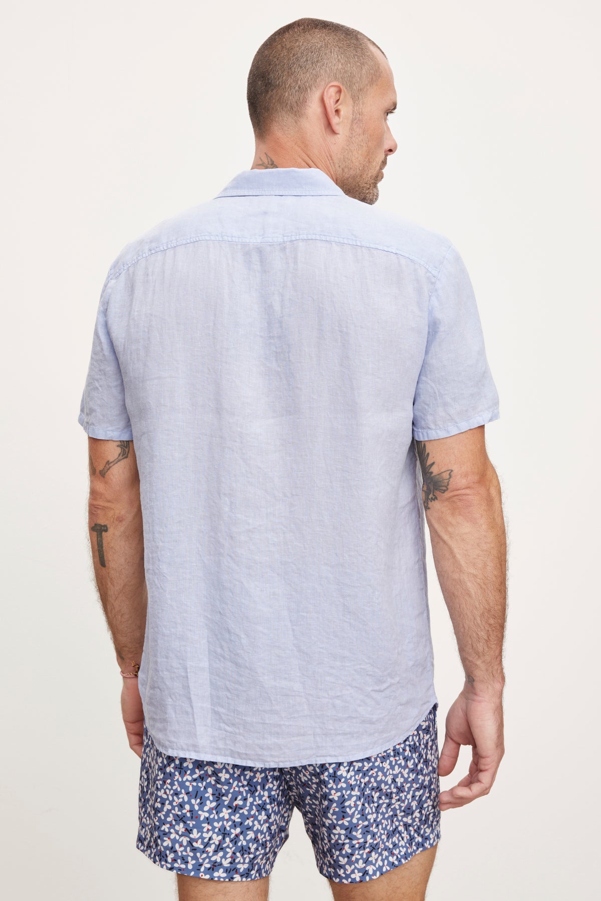 A man seen from behind wears a Velvet by Graham & Spencer MACKIE LINEN BUTTON-UP SHIRT and patterned shorts, standing against a white background.-36753546346689