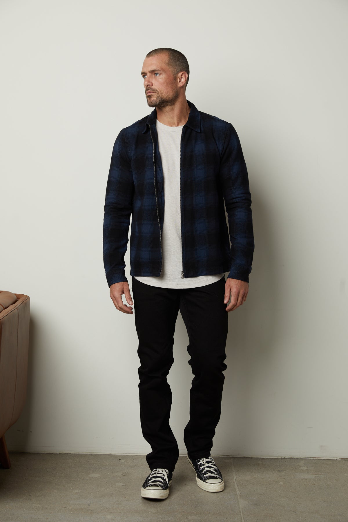 A man wearing a Velvet by Graham & Spencer MARK ZIP-UP PLAID SHIRT and black pants in front of a wall.-35231562268865