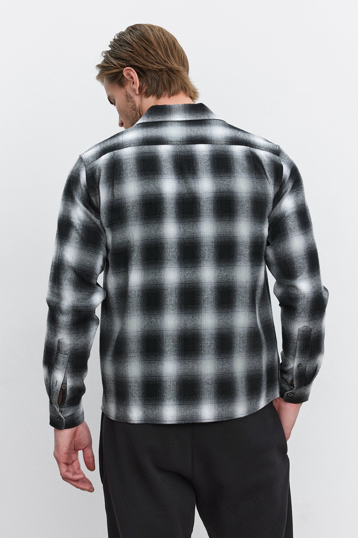   A person with light brown hair is wearing the Velvet by Graham & Spencer STANTON BUTTON-UP SHIRT in a black and white plaid ombre design, viewed from the back. 