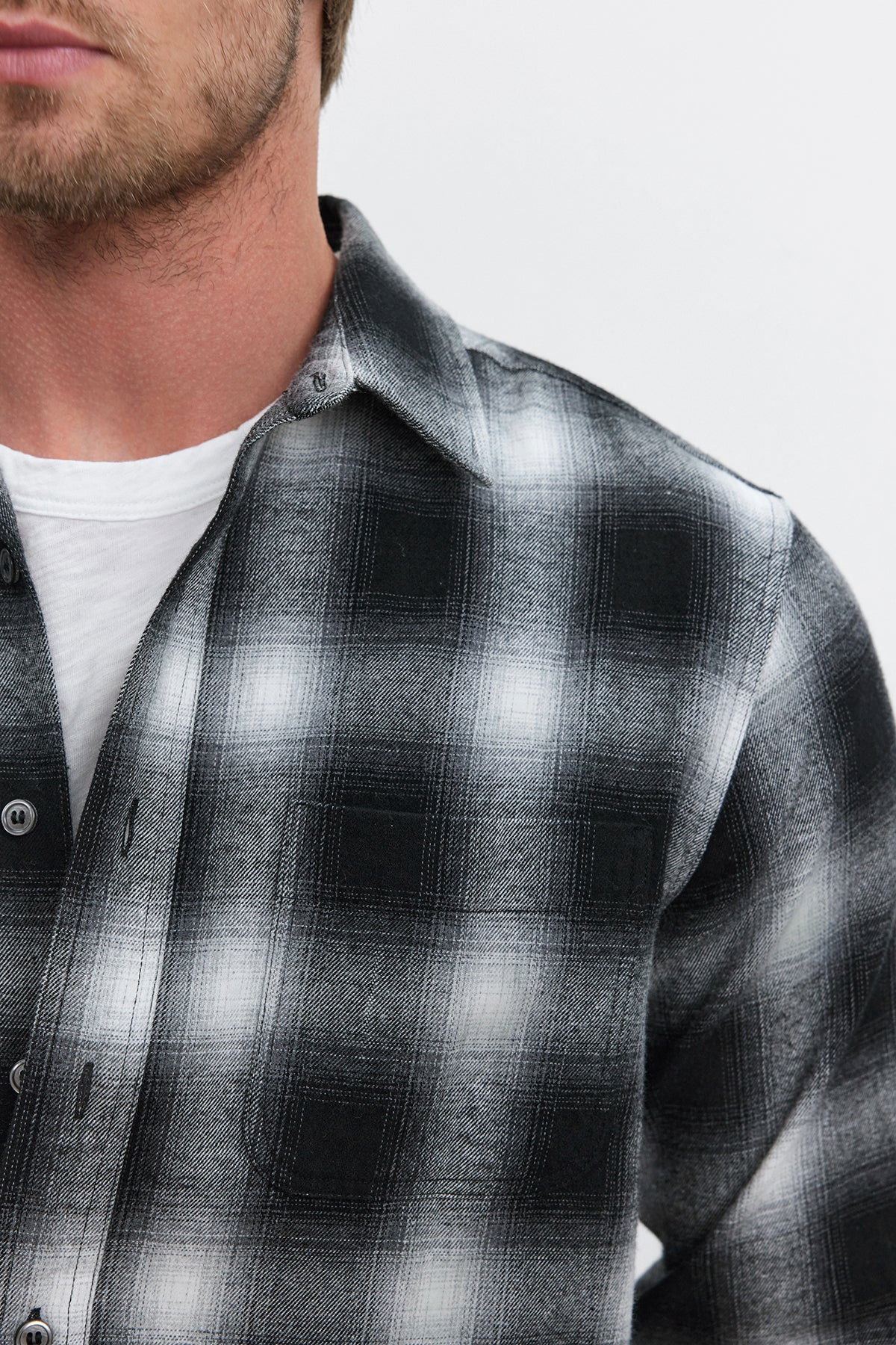 Close-up of a person wearing the Velvet by Graham & Spencer STANTON BUTTON-UP SHIRT over a white T-shirt. The image captures the plaid ombre design of the black and white cotton flannel shirt and part of the person's face and neck.-37893756354753