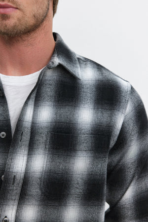 Close-up of a person wearing the Velvet by Graham & Spencer STANTON BUTTON-UP SHIRT over a white T-shirt. The image captures the plaid ombre design of the black and white cotton flannel shirt and part of the person's face and neck.