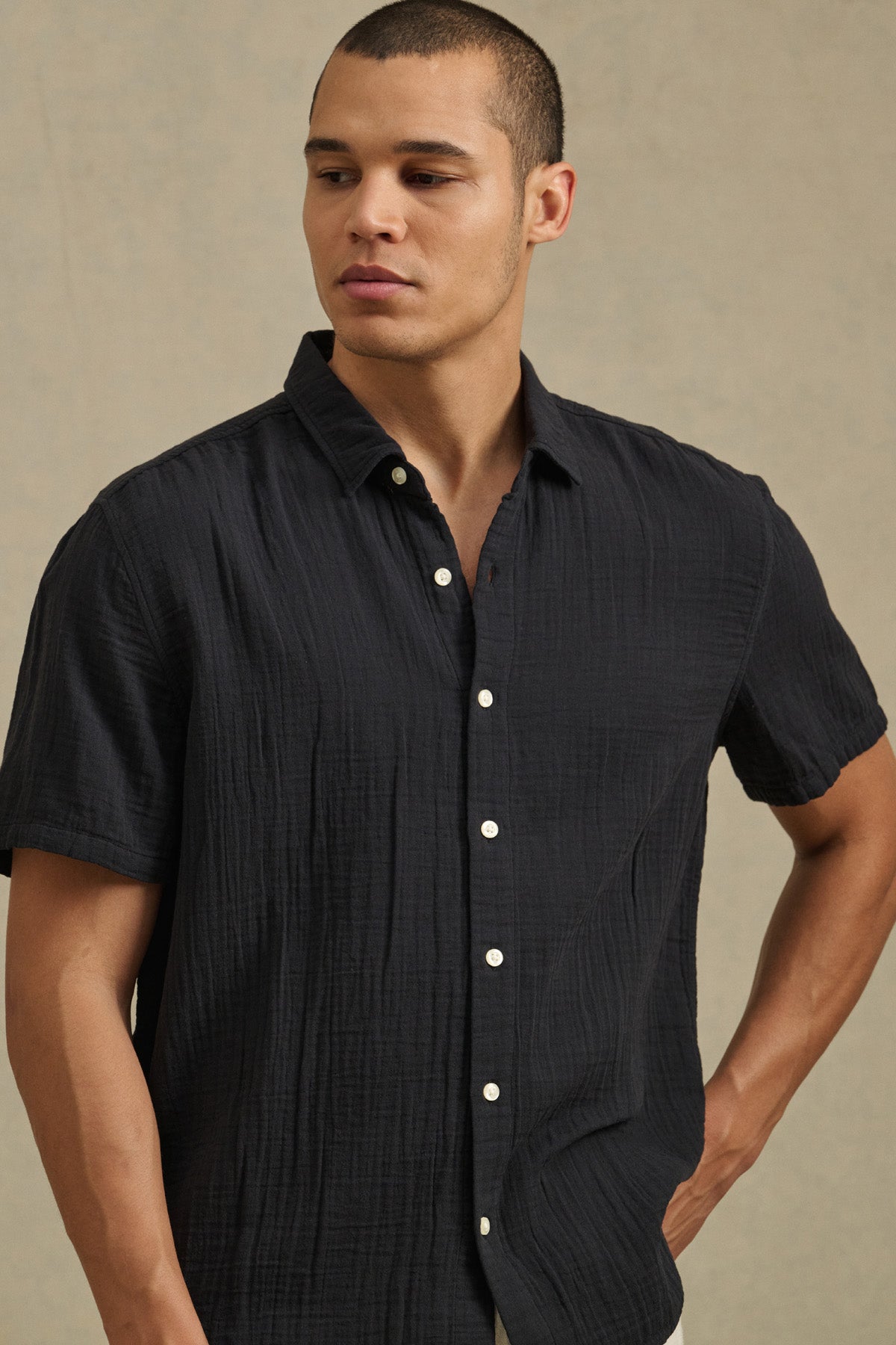 Wearing the Velvet by Graham & Spencer TROY SHIRT, a person stands against a plain beige background, gazing slightly to the side.-41428172603585