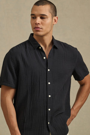 Wearing the Velvet by Graham & Spencer TROY SHIRT, a person stands against a plain beige background, gazing slightly to the side.