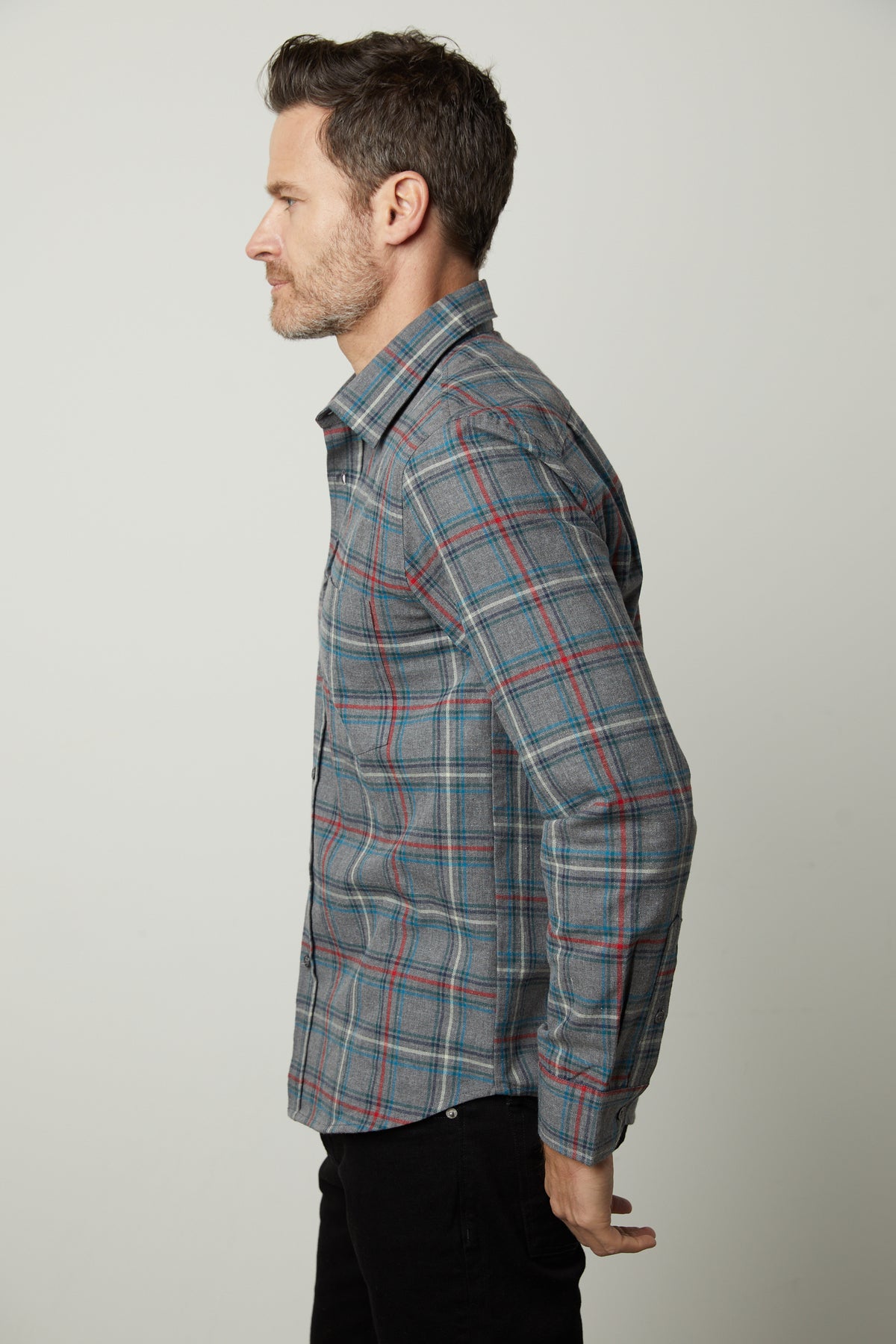   A man in a WILDER PLAID BUTTON-UP SHIRT by Velvet by Graham & Spencer stands in profile against a plain background, with his hands clasped behind his back. 