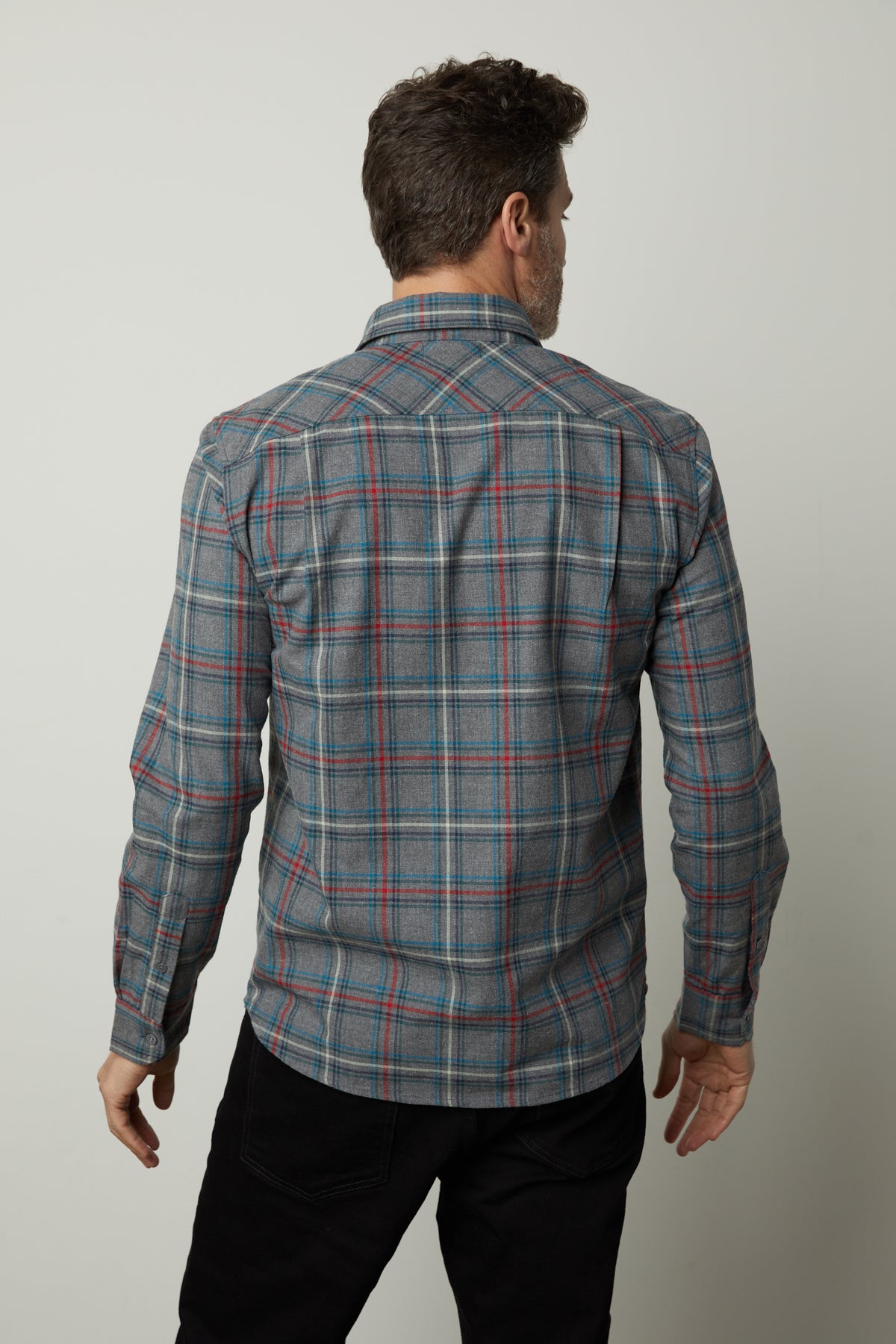   A man is standing with his back to the camera, showcasing the WILDER PLAID BUTTON-UP SHIRT by Velvet by Graham & Spencer, which features a grey and blue plaid pattern and is made from lightweight cotton. He pairs the shirt with black pants against a plain white background. 