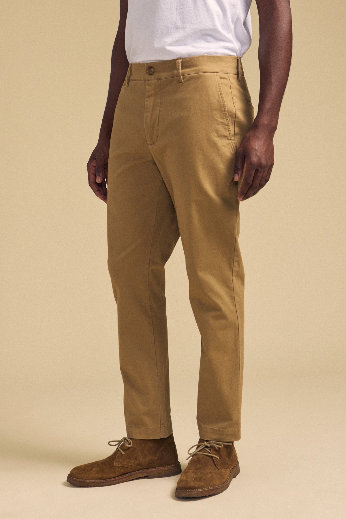 A person wearing the LUIS CHINO by Velvet by Graham & Spencer, a white t-shirt, and brown suede shoes stands against a beige background.