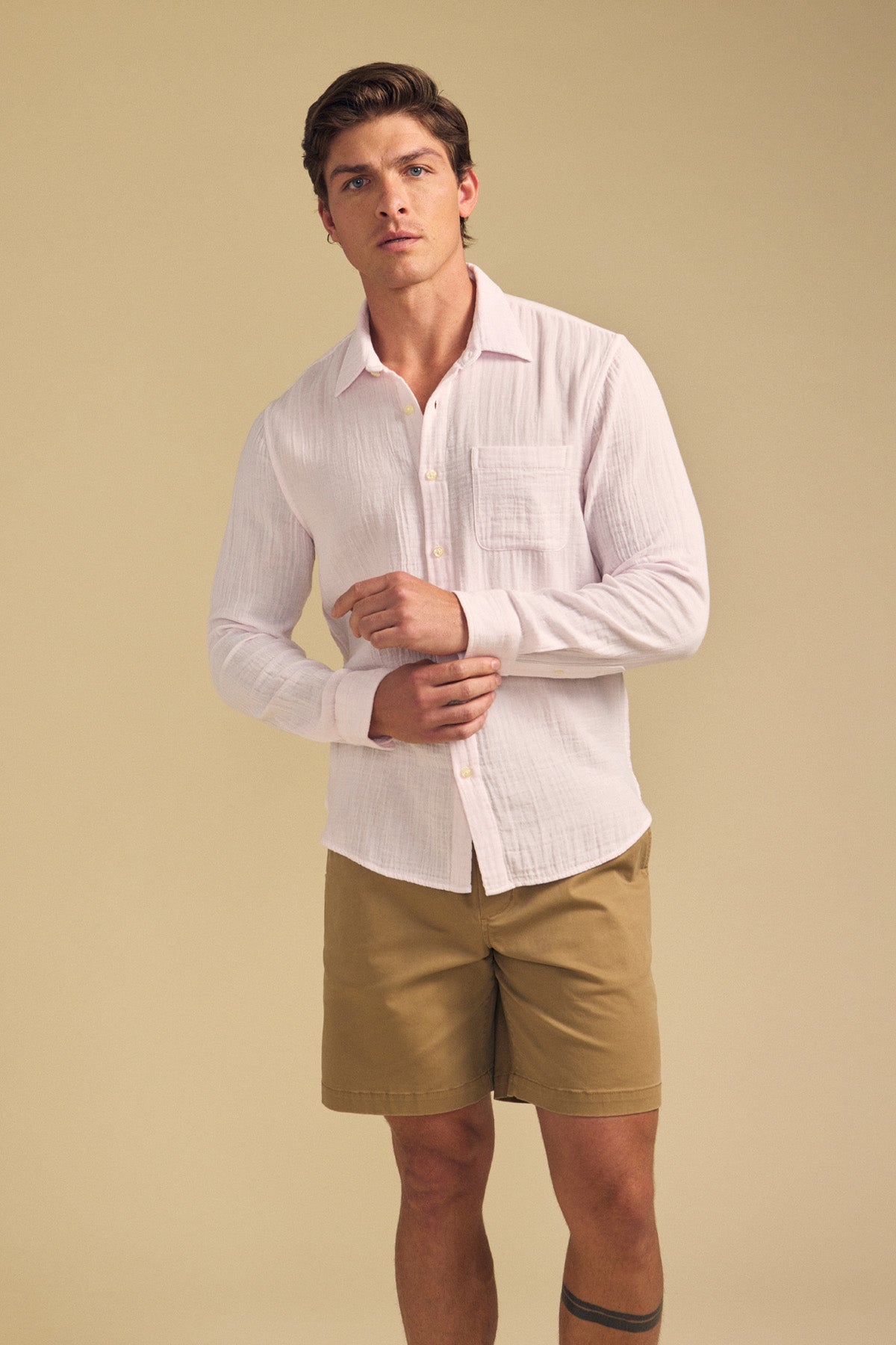 A man stands against a beige background wearing the light pink APOLLO SHIRT by Velvet by Graham & Spencer and khaki shorts.-41701729730753