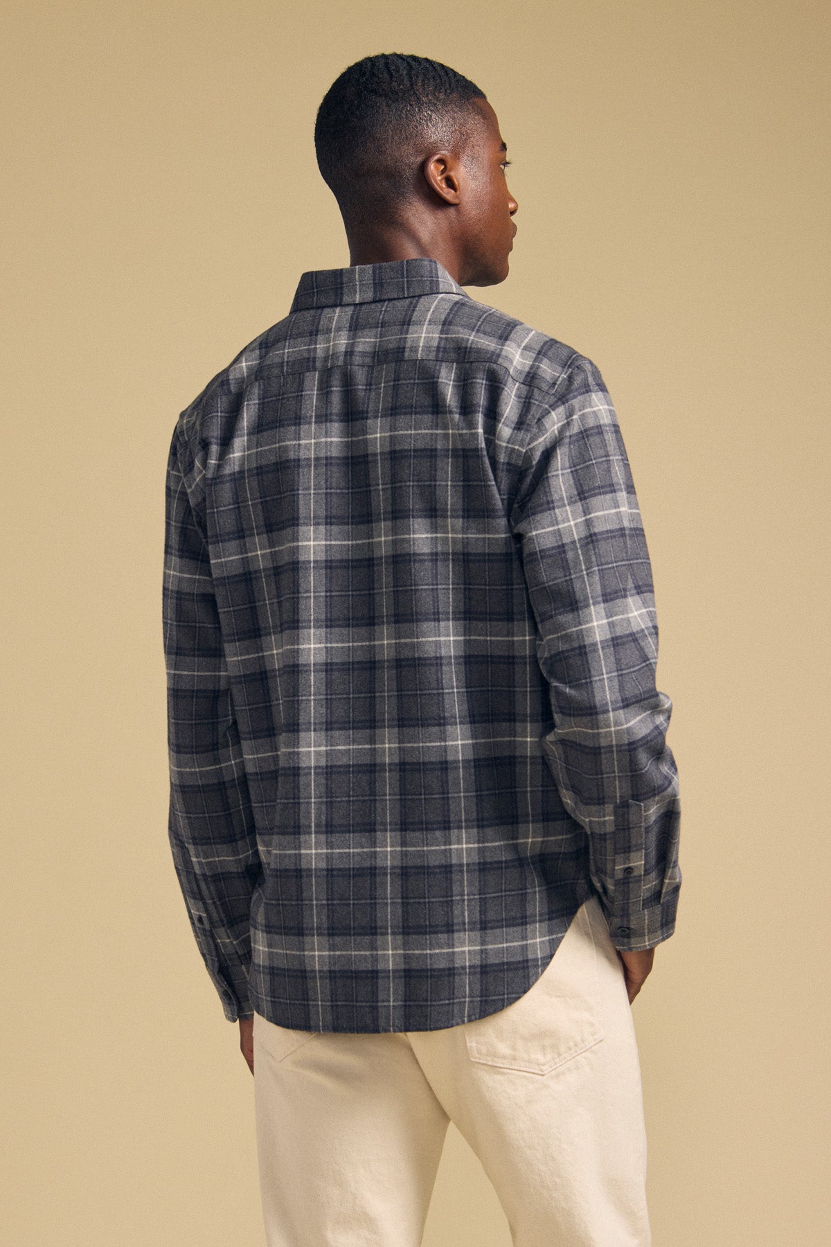 A person stands with their back to the camera, wearing the COLE SHIRT in a gray plaid flannel by Velvet by Graham & Spencer, paired with light-colored pants against a plain beige background.