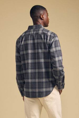 A person stands with their back to the camera, wearing the COLE SHIRT in a gray plaid flannel by Velvet by Graham & Spencer, paired with light-colored pants against a plain beige background.