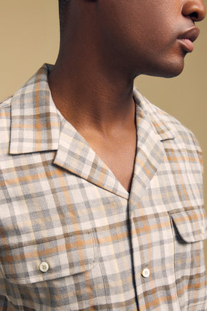 A person wearing the Velvet by Graham & Spencer CUB SHIRT, a light plaid button-up with a notched collar, photographed from the shoulders up against a plain beige background.