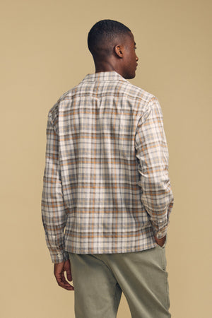 A man stands facing away, wearing the CUB SHIRT by Velvet by Graham & Spencer in a beige and gray plaid, paired with light olive pants against a plain beige background.