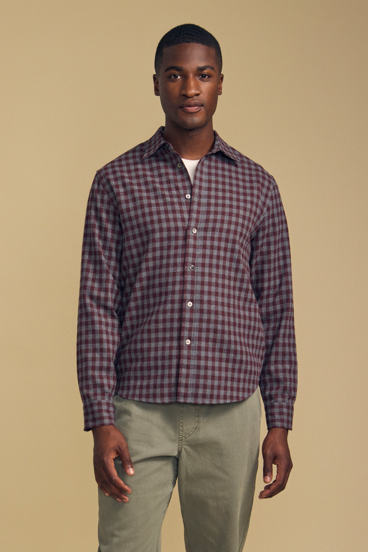 A man wearing a burgundy and gray DANNY PLAID BUTTON-UP SHIRT over a white undershirt and olive pants.