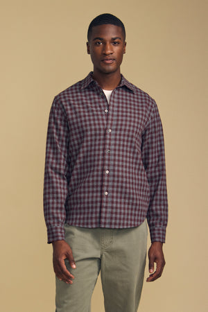 A man wearing a burgundy and gray DANNY PLAID BUTTON-UP SHIRT over a white undershirt and olive pants.