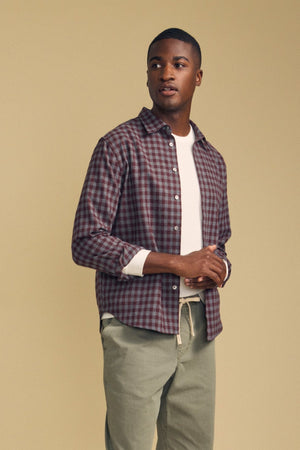 A person wears a burgundy and navy DANNY PLAID BUTTON-UP SHIRT by Velvet by Graham & Spencer over a white neutral polo, paired with olive green pants.