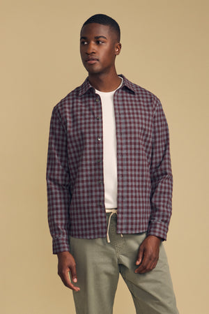 A person wearing a DANNY PLAID BUTTON-UP SHIRT in burgundy and grey over a white neutral pique knit polo.