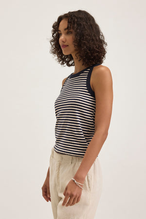 A person with curly hair wears the LUA TANK TOP, a black and white striped sleeveless piece by Velvet by Graham & Spencer, paired with beige pants against a plain background.