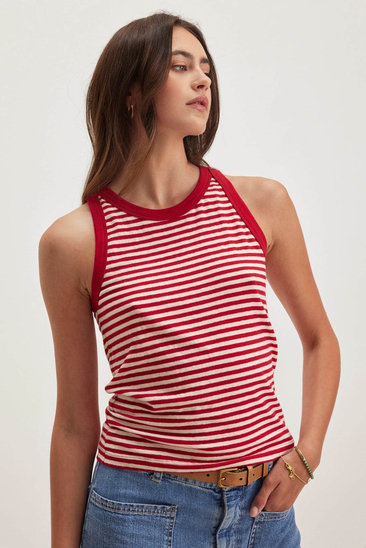   A person is wearing the LUA TANK TOP by Velvet by Graham & Spencer, featuring red and white stripes, paired with jeans. They are looking sideways with arms relaxed. 