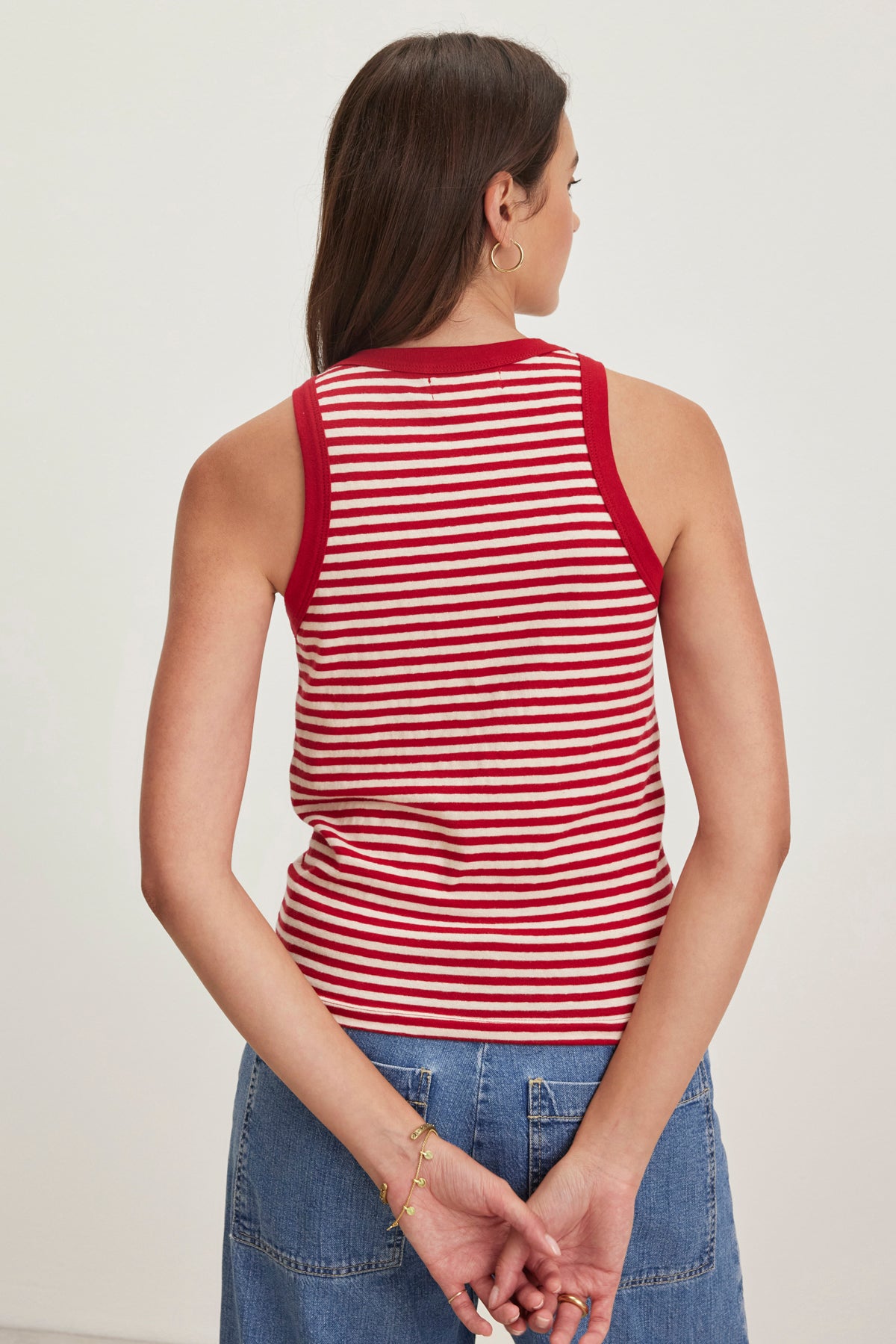   A brown-haired woman in a Velvet by Graham & Spencer LUA red and white striped tank top and denim skirt stands with her hands clasped behind her back, facing away. 