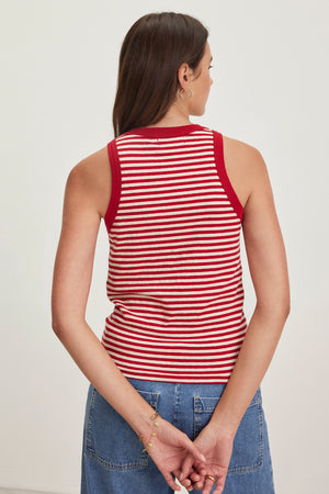 A brown-haired woman in a Velvet by Graham & Spencer LUA red and white striped tank top and denim skirt stands with her hands clasped behind her back, facing away.