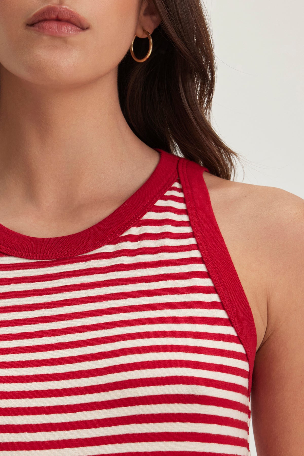   A woman in a LUA TANK TOP by Velvet by Graham & Spencer, featuring red and white stripes with red trim, has long brown hair and wears gold hoop earrings. 