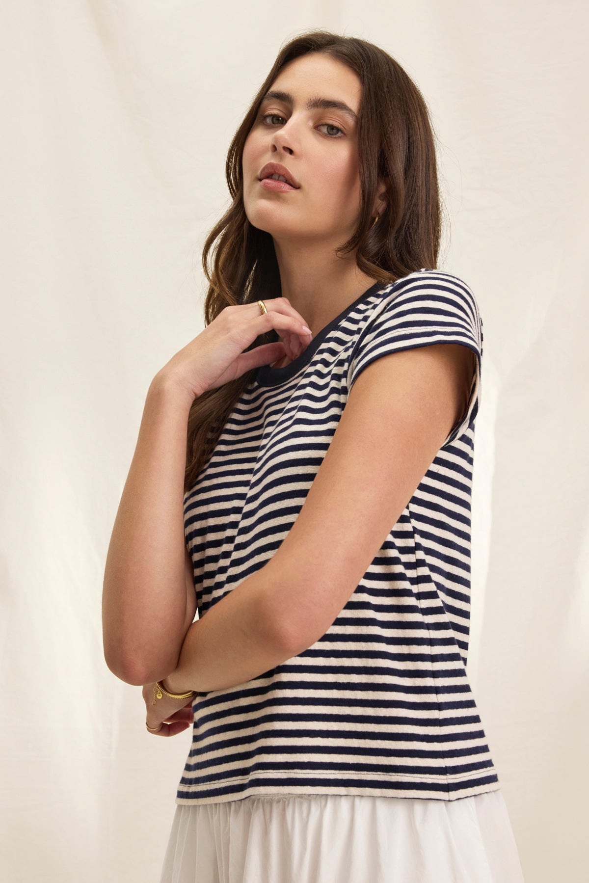 A person poses against a plain background wearing the TASH TEE from Velvet by Graham & Spencer, featuring a classic crew neckline and stripes, paired with a white skirt for a comfortable yet chic boxy fit.-38820850303169