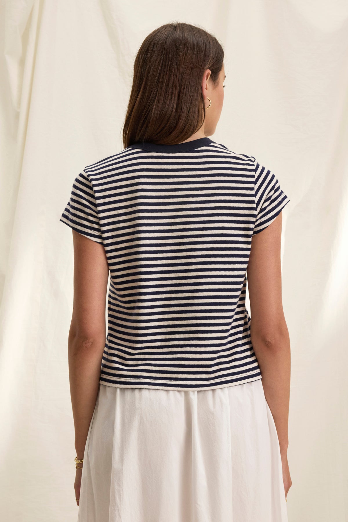 A person with long hair, wearing the TASH TEE by Velvet by Graham & Spencer and a white skirt, stands with their back to the camera against a cream background.-38820850237633