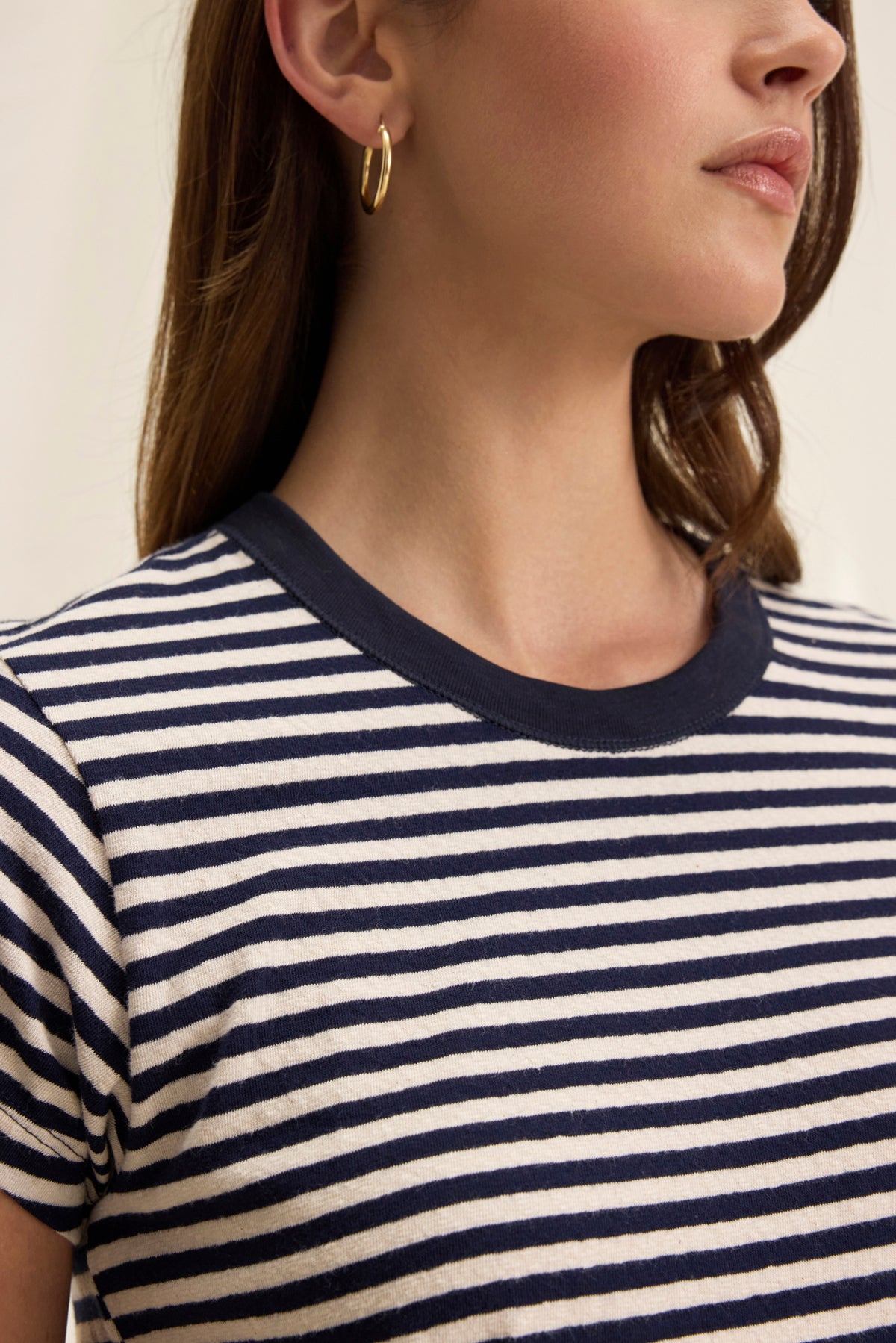 A person in a TASH TEE by Velvet by Graham & Spencer (black and white striped cotton jersey shirt with a crew neckline) is facing slightly to the side, wearing a gold hoop earring.-38820850106561