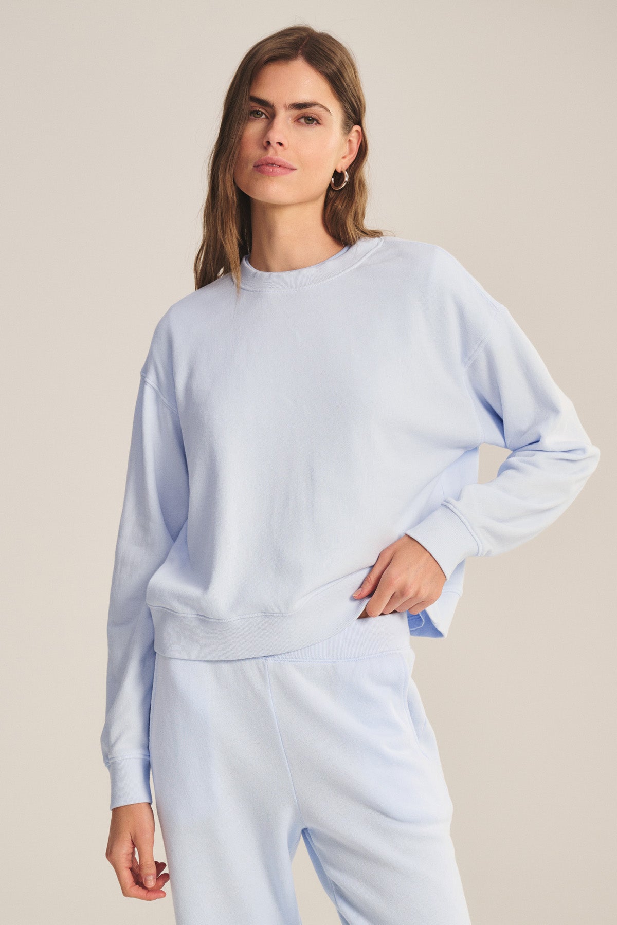 A woman models the YOKO SWEATSHIRT by Velvet by Graham & Spencer with matching light blue cotton fleece sweatpants, standing against a plain background and highlighting the relaxed fit.-41044199735489