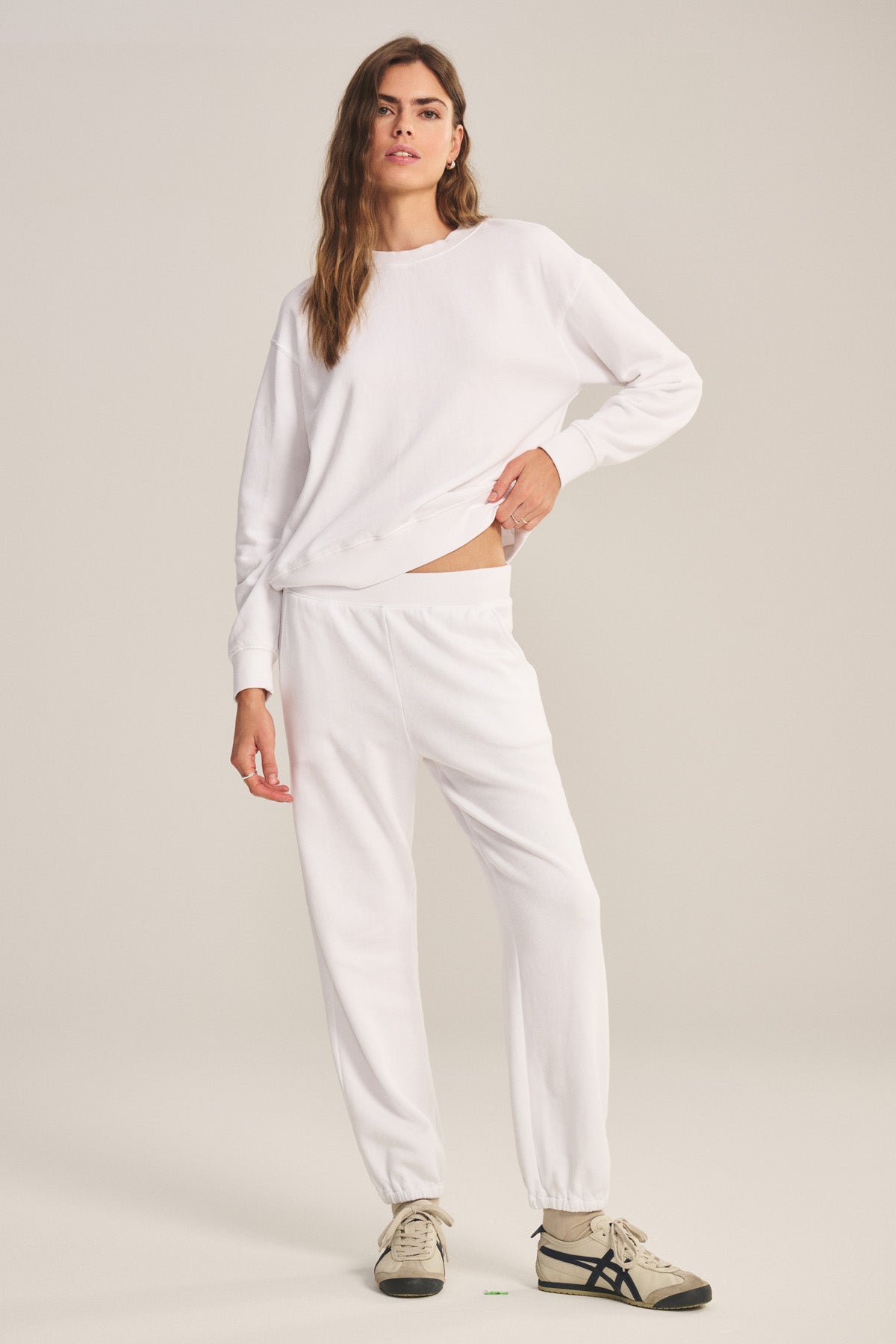 A person stands against a plain background wearing the YOKO SWEATSHIRT by Velvet by Graham & Spencer, paired with matching white sweatpants and beige sneakers.-40293969199297