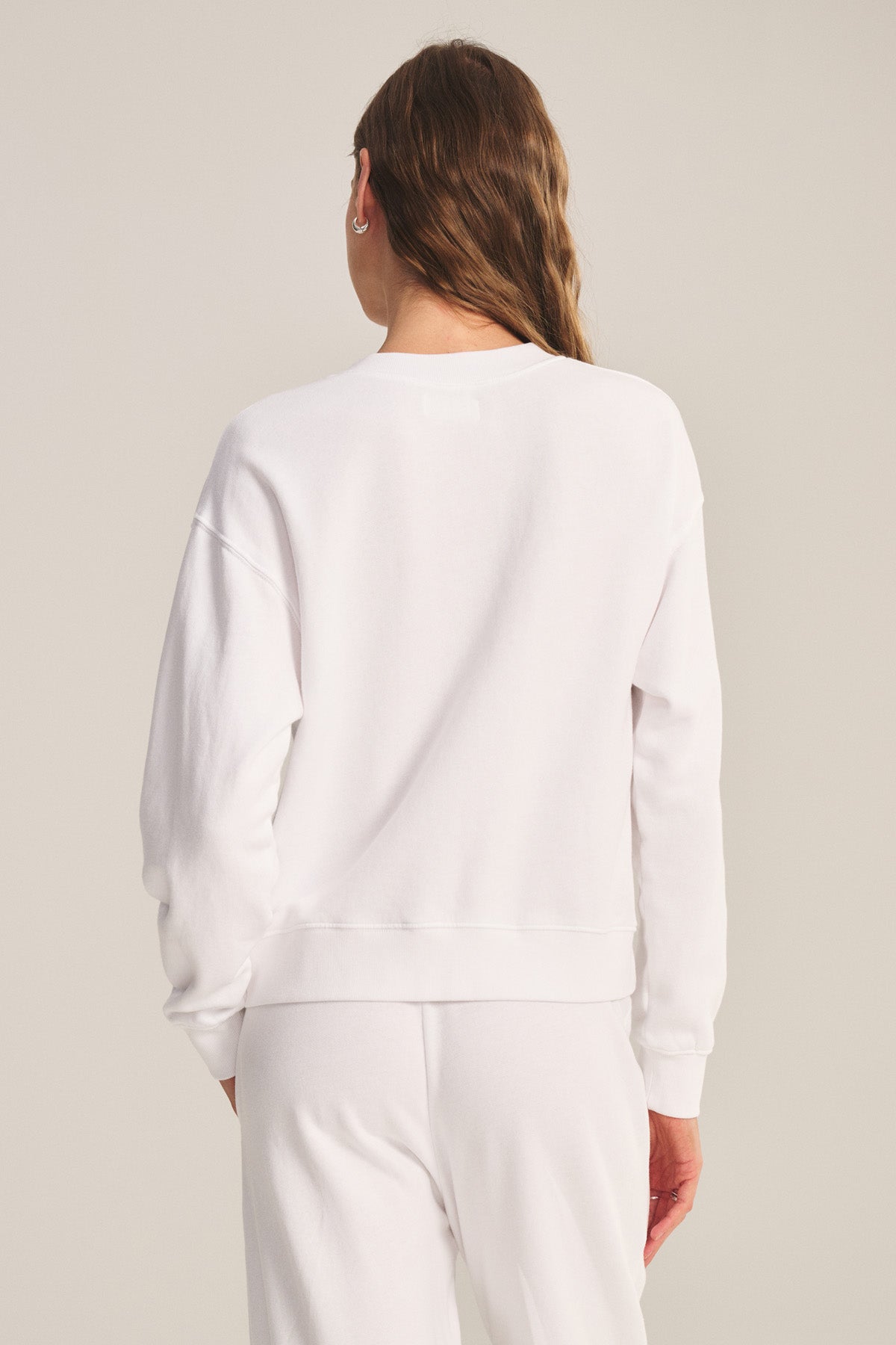 A person stands facing away, wearing the Velvet by Graham & Spencer YOKO SWEATSHIRT and matching white pants against a plain background.-40293970706625