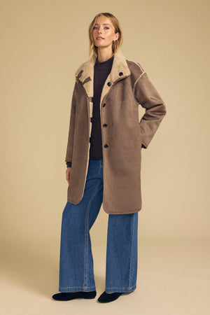 A woman models the YVES FAUX SUEDE FUR REVERSIBLE COAT by Velvet by Graham & Spencer, layered over a dark top and wide-leg blue jeans, set against a plain beige background.
