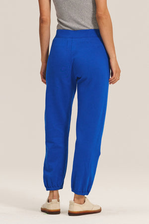 A person is shown from the back in a grey short-sleeve top, relaxed fit bright blue ZARA SWEATPANT by Velvet by Graham & Spencer in soft cotton fleece, and beige shoes against a plain background.