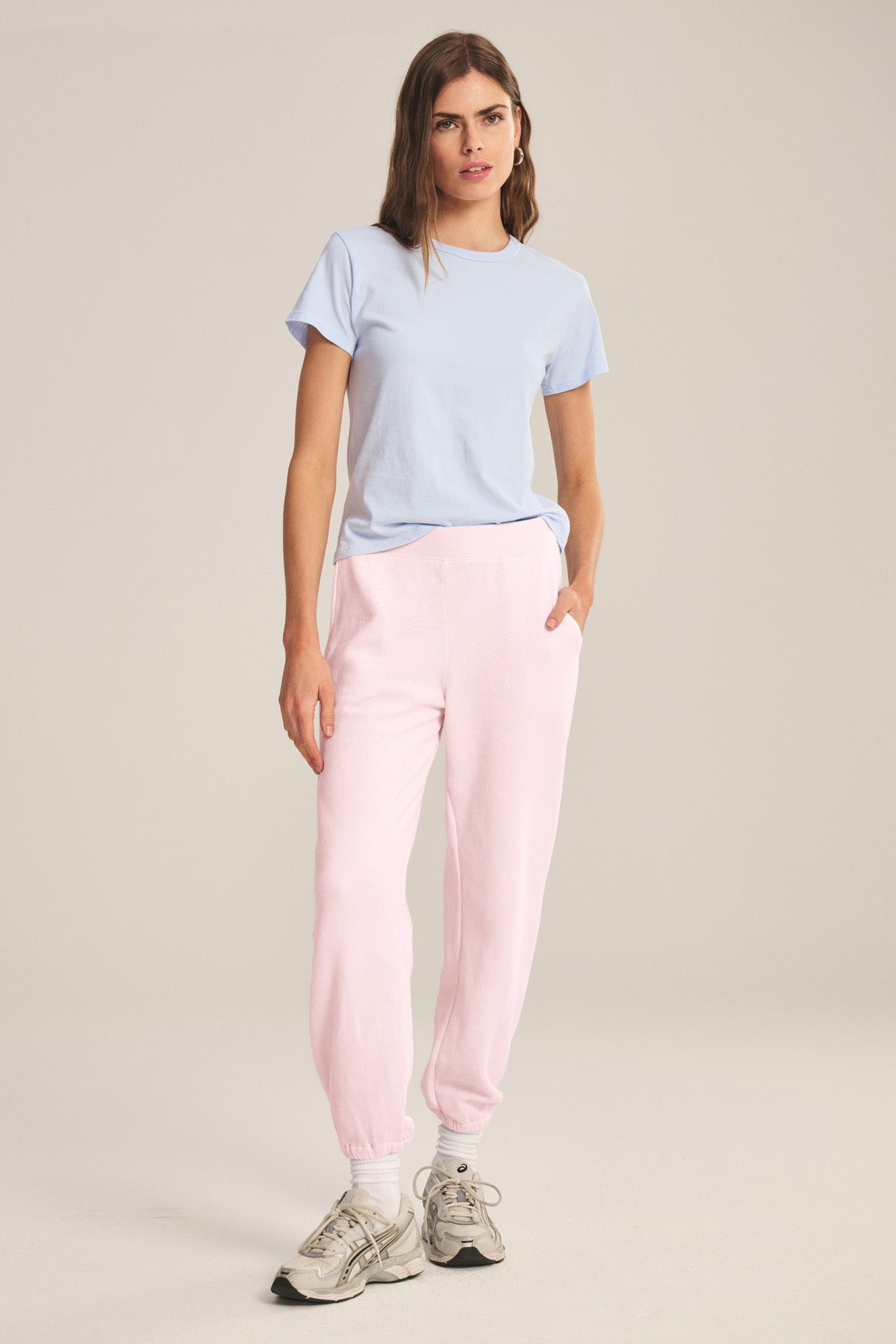 A person stands facing forward, wearing a light blue t-shirt, Velvet by Graham & Spencer ZARA SWEATPANT in relaxed fit pink cotton fleece, and white sneakers against a plain background.-41044338278593