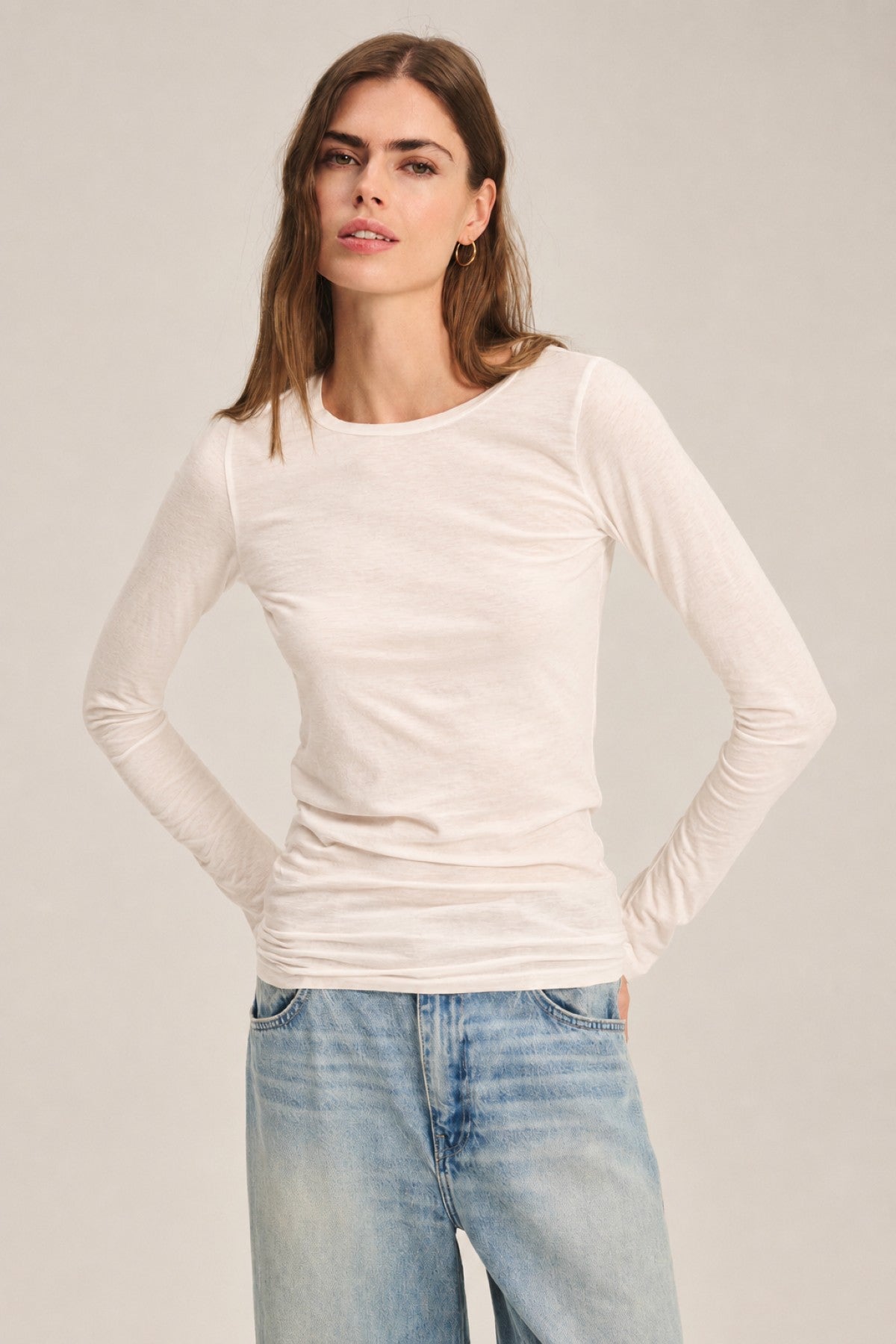 A woman stands with her hands in her pockets against a neutral background, wearing the Velvet by Graham & Spencer ZOFINA TEE—an ultra-soft, gauzy whisper fitted long sleeve tee with a classic crew neckline—paired with light blue jeans.-41781415051457