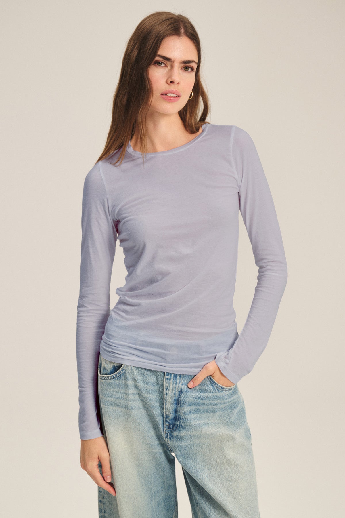 A woman stands against a plain background wearing the Velvet by Graham & Spencer ZOFINA TEE in light purple with light blue jeans.