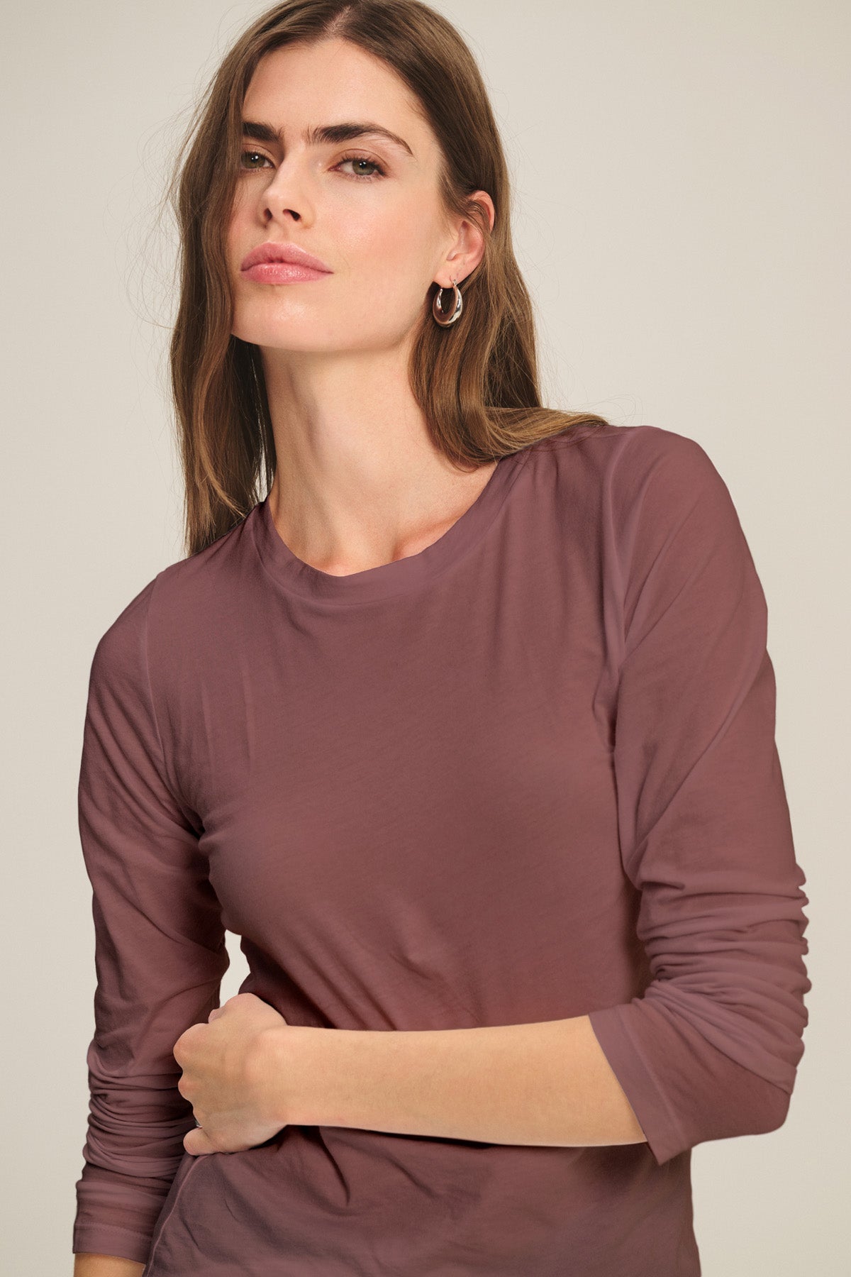 A woman with long brown hair wears the ultra-soft ZOFINA TEE by Velvet by Graham & Spencer, featuring a fitted long sleeve and crew neckline, as she looks at the camera against a plain background.