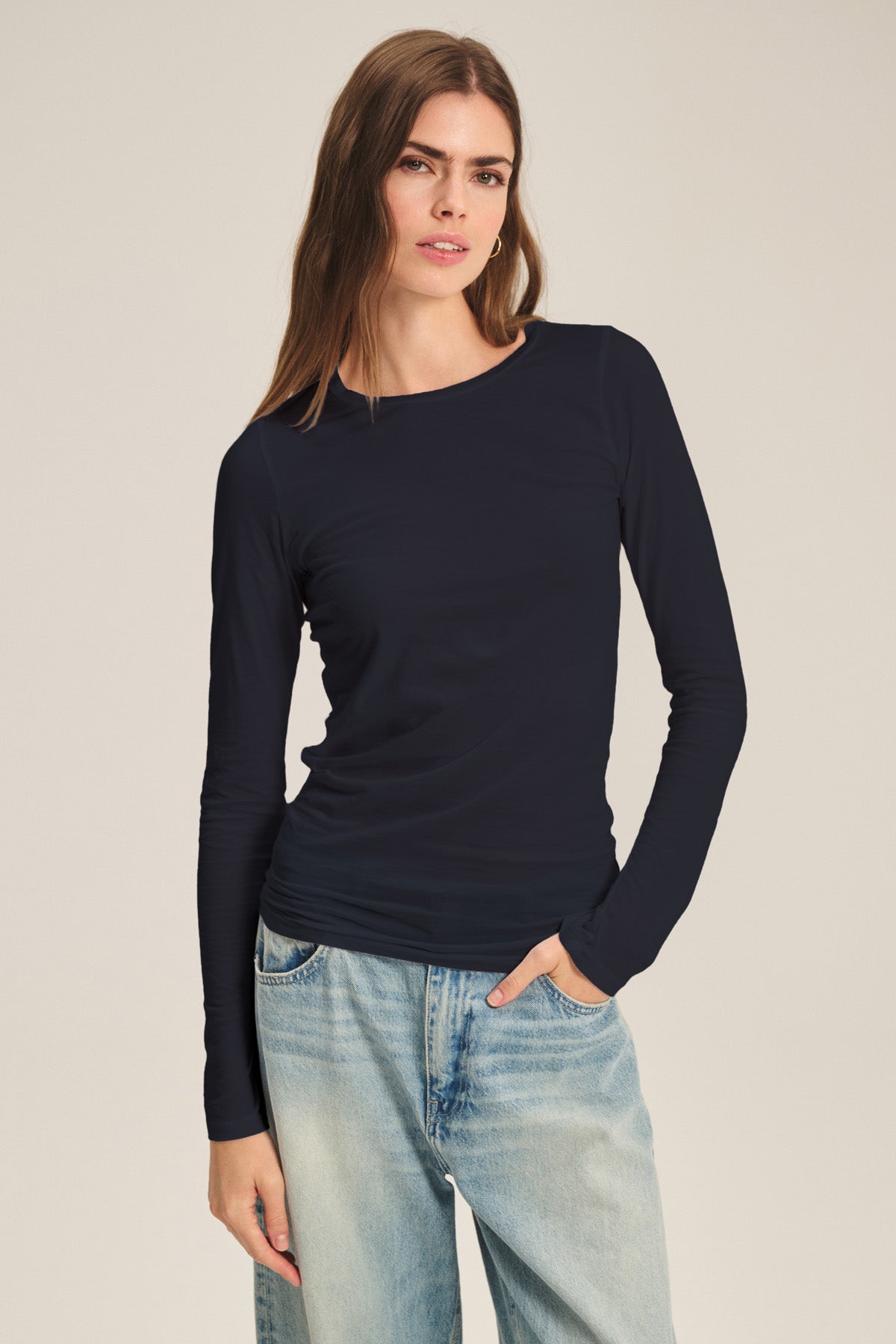 A person wearing the ZOFINA TEE by Velvet by Graham & Spencer, an ultra-soft fitted long sleeve crewneck, pairs it with light blue jeans and stands against a plain, light background.-40807729529025