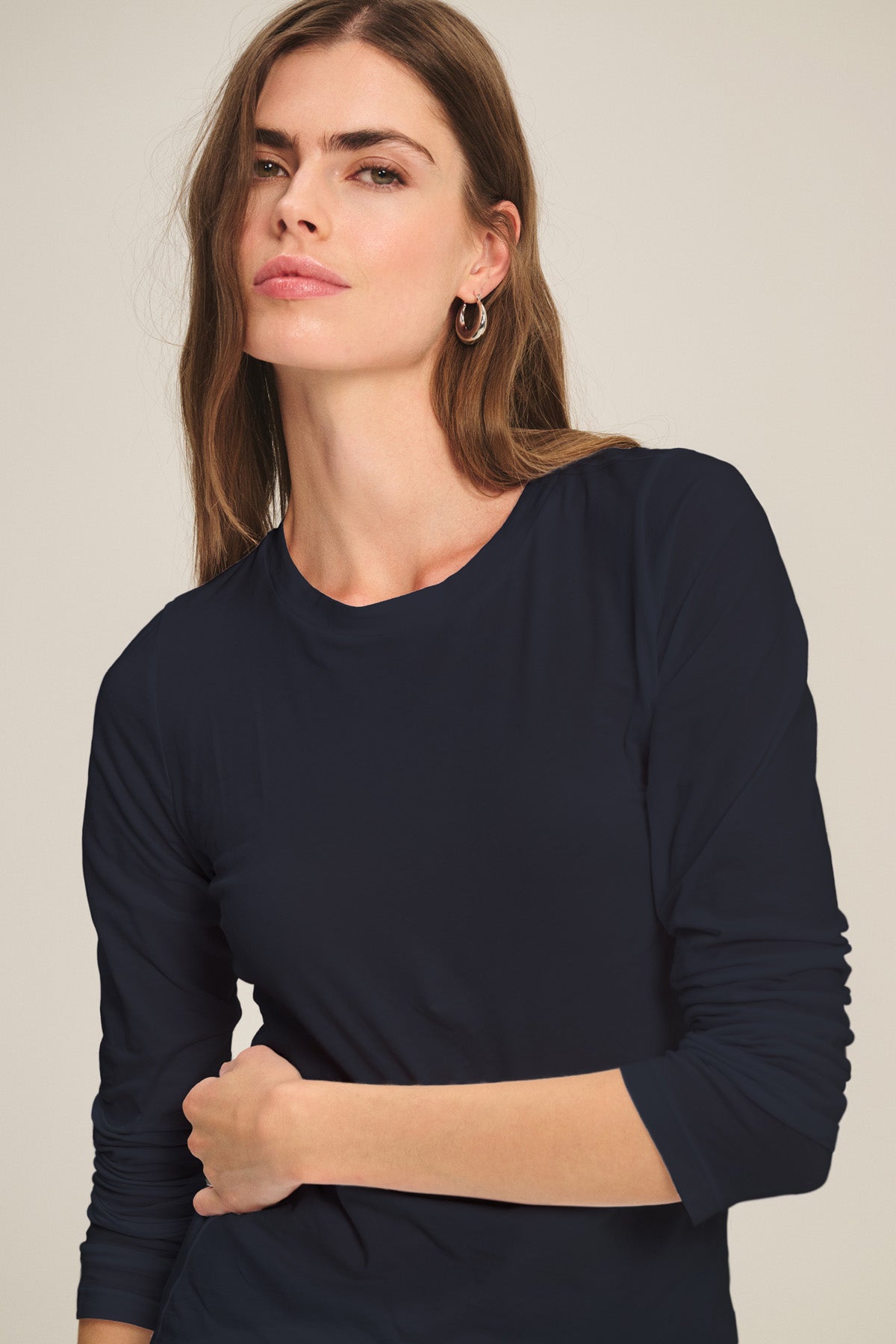 A woman with long brown hair models the ZOFINA TEE by Velvet by Graham & Spencer, an ultra-soft gauzy whisper fitted long sleeve crewneck, standing against a plain light background.-40807729496257