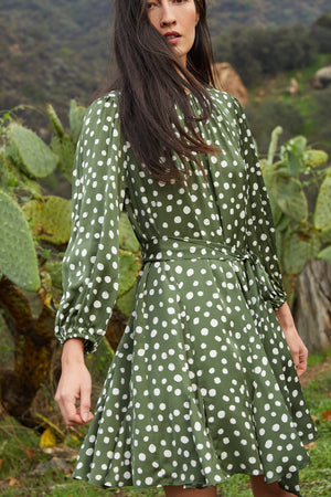 Model standing outside wearing Kenia Polka Dot Dress with Green Background and Cream Dots front view tied at waist