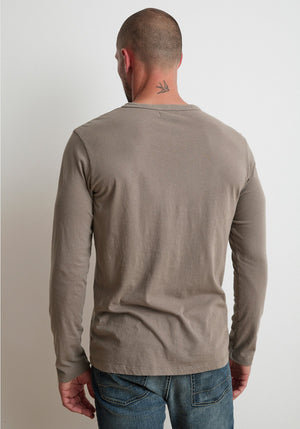 A person with a shaved head, standing with their back to the camera, wearing a gray ALVARO HENLEY by Velvet by Graham & Spencer and blue jeans. A small tattoo is visible on the back of their neck.