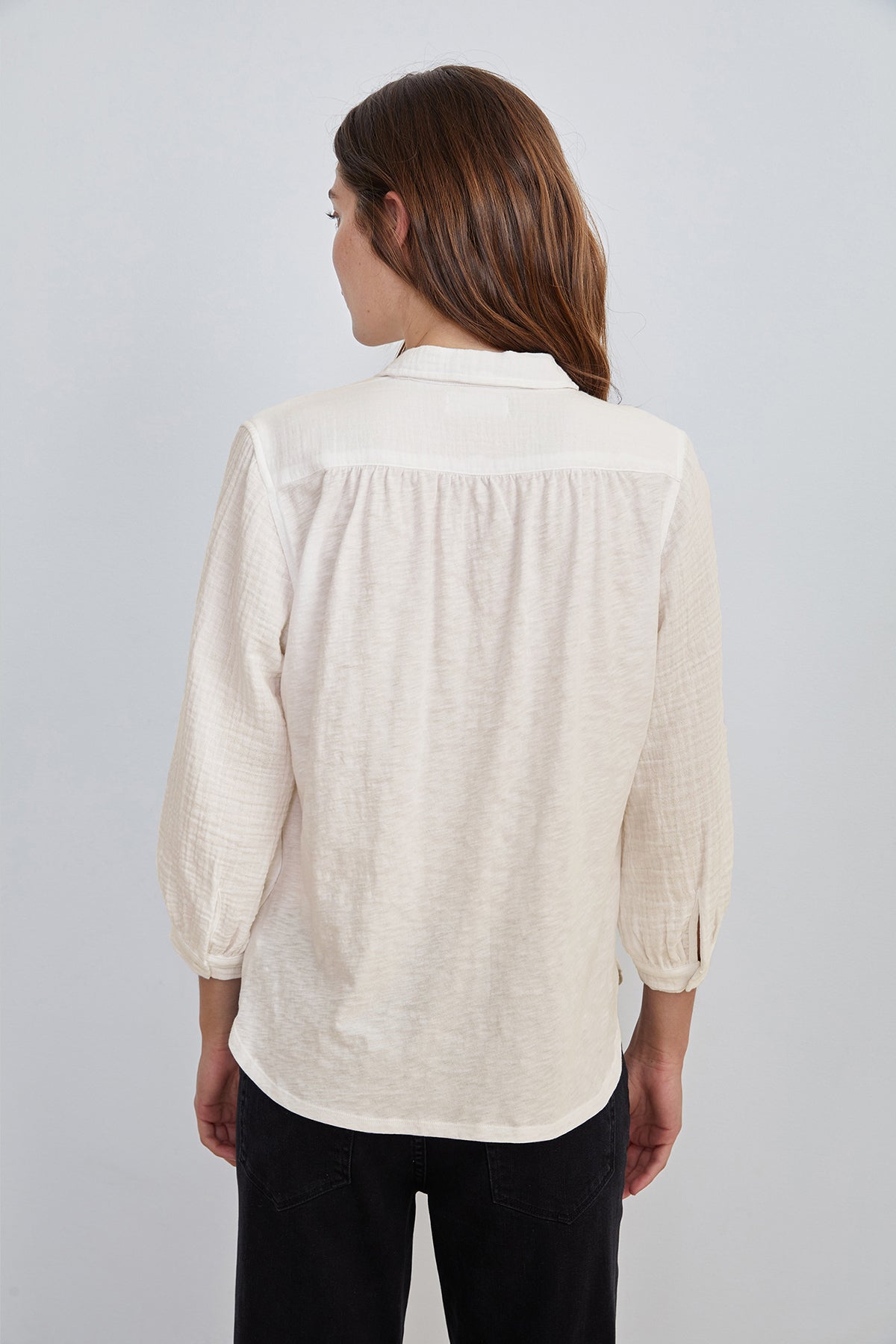 A woman with long brown hair, seen from the back, is wearing the Velvet by Graham & Spencer DAYNA 3/4 Sleeve Button-Up Blouse in lightweight cotton slub along with dark pants against a plain background.-14906065846465