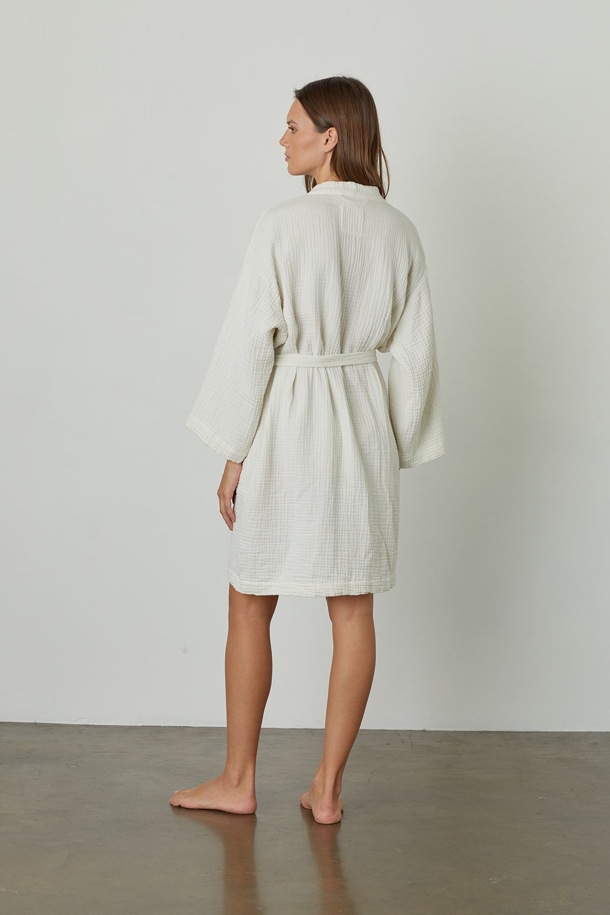 The back view of a woman wearing a MINI COTTON GAUZE ROBE made by Jenny Graham Home, with soft texture.-23555997532353